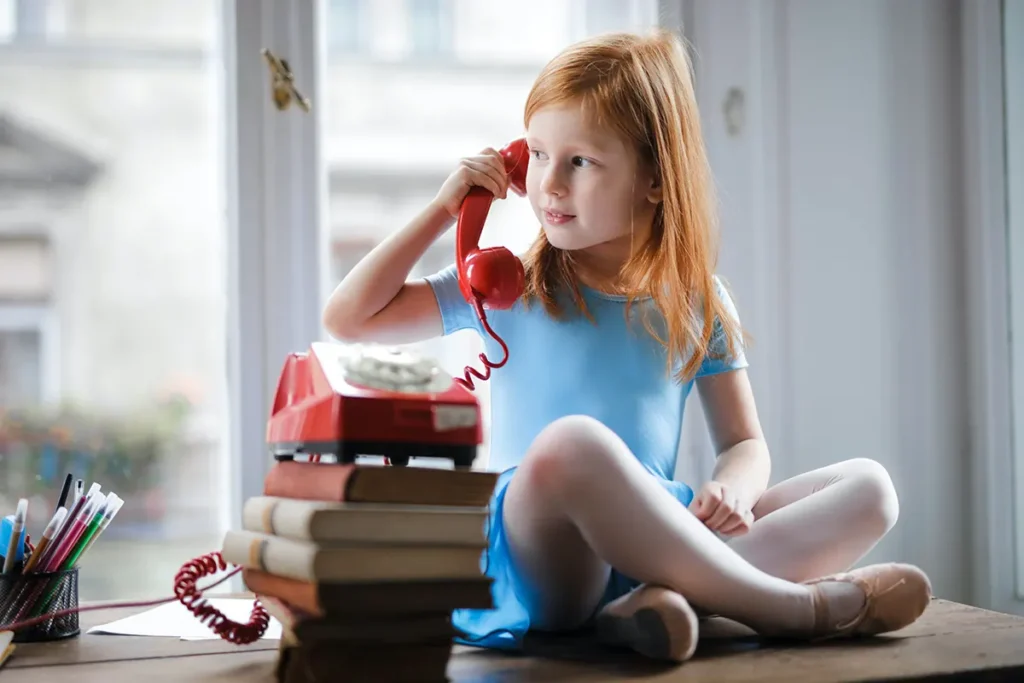bambina con i capelli rossi che telefona con un telefono rosso