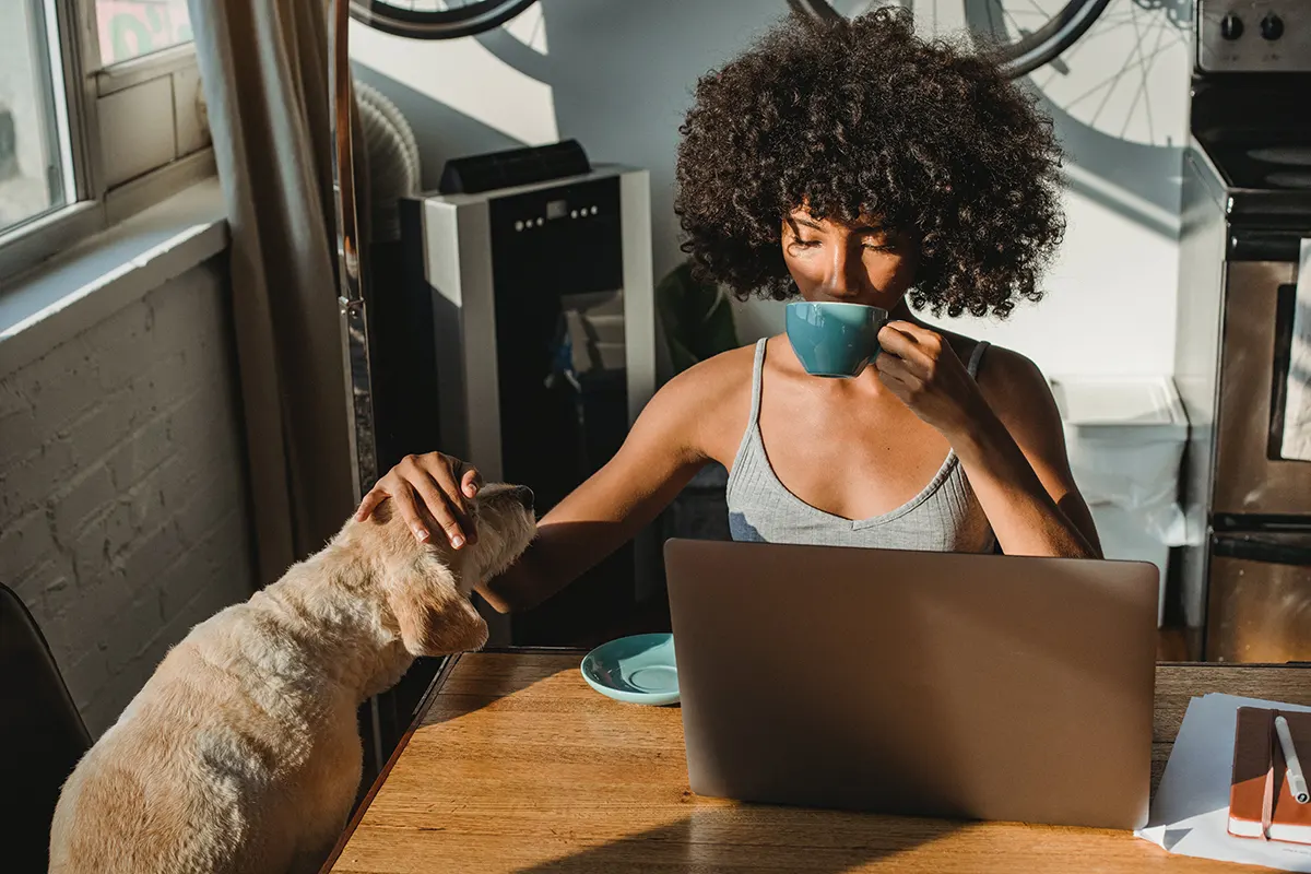 donna al computer che beve una tazza di caffè e accarezza un cane